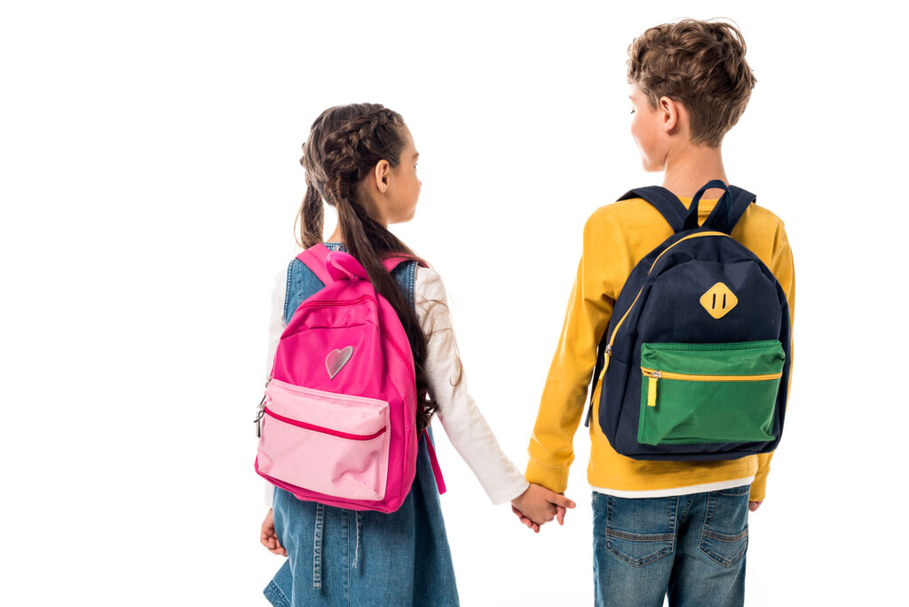 two kids holding hands wearing backpacks